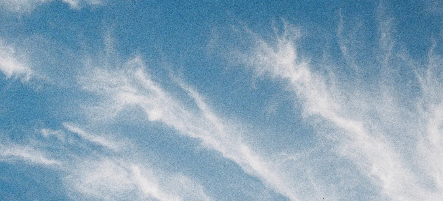 Lines of wispy clouds move upward and to the left against a backdrop of light blue sky