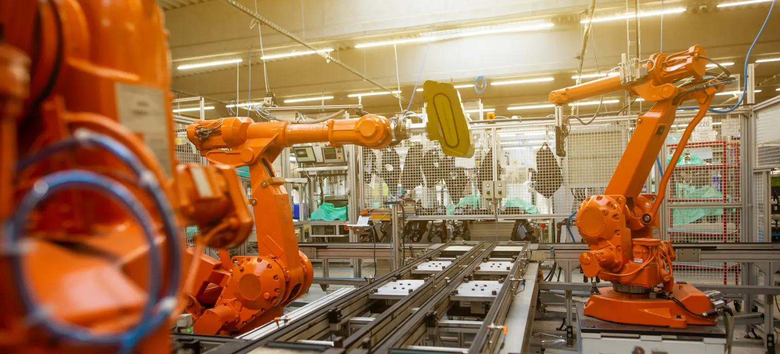 Several robotic arms sit perched over mechanical tracks in a factory, ready to do some type of assembly.