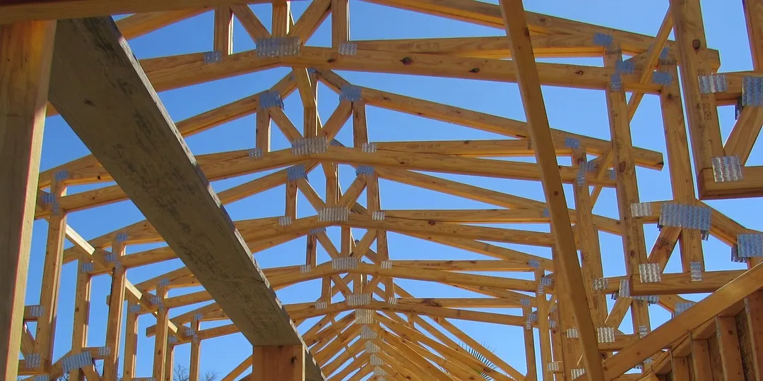 A view upward toward the wooden framing of a house under construction against a blue sky.