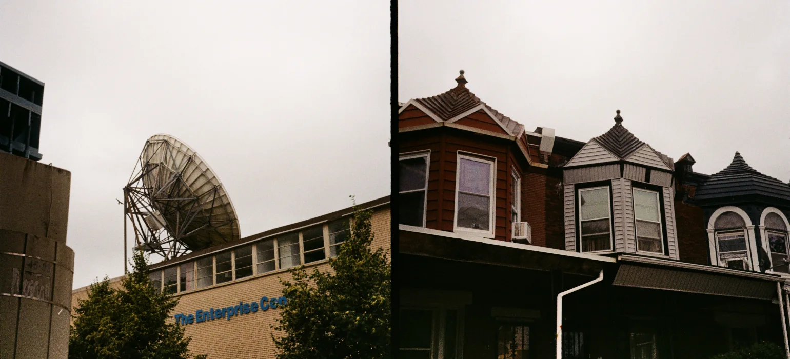 On the left, a 70s-era yellow brick building with a satellite dish on top is seen from below, rising above the tops of two green trees. On the right, split by a thin black line, are three houses with distinct bay window facade toppers on their second stories.