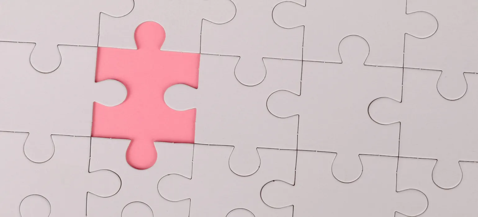 A blank jigsaw puzzle with one piece missing, revealing pink beneath.
