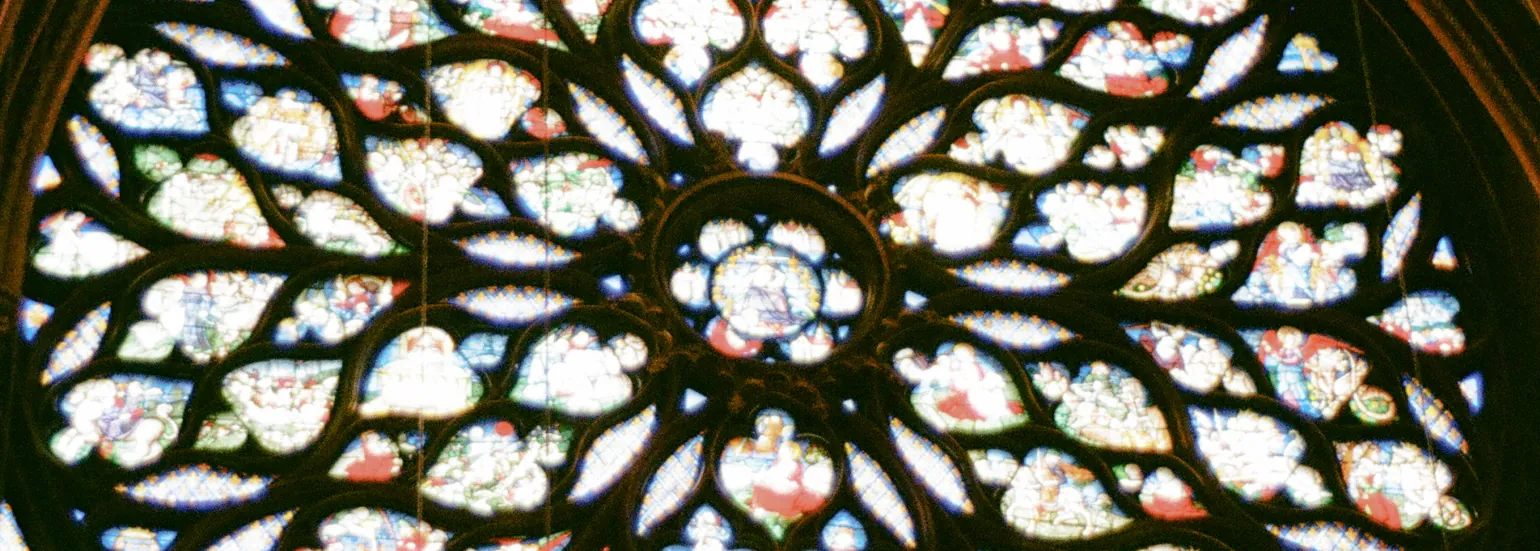 An ornate pattern flowers out from a circular window in the center of the image, framing plant-shaped stained glass depicting European church images
