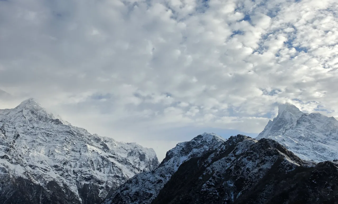 A panoramic view from a mountain overlooks a vast valley stretching to the horizon under a stormy sky.